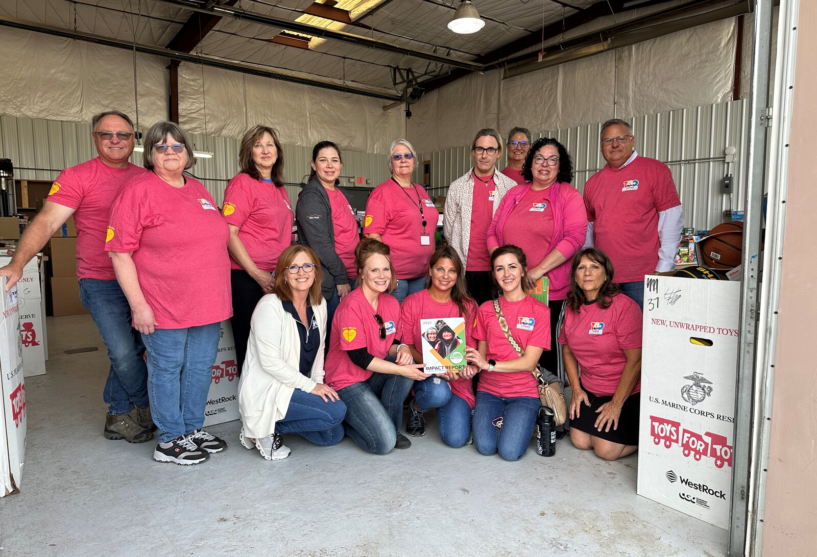 employees in pink shirts pose inside warehouse