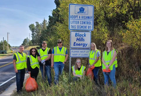 Group of employees standing next to a sign by the road