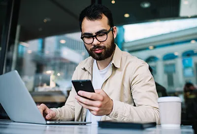 Person holding a smartphone while working on a laptop.