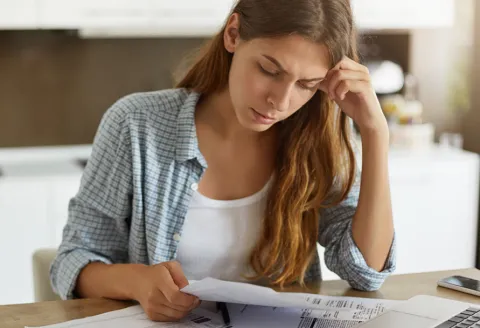 Woman looking over papers while sitting at the table and looking concerned