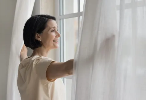 Woman in front a window opening white curtains