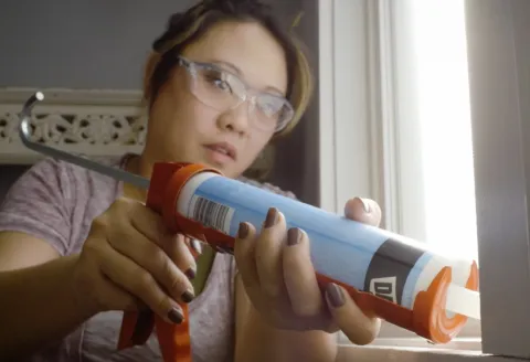 Woman caulking a window