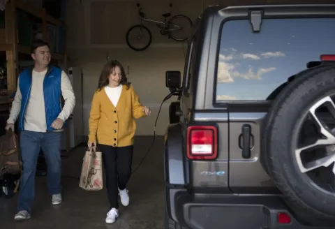 A man and a woman in the garage walking towards their EV vehicle
